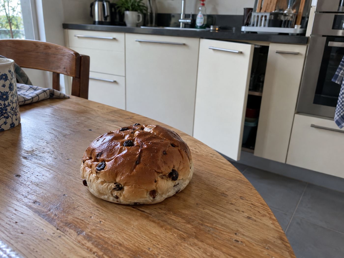 Een krentenbol op de keukentafel, met een keukenkastje op een kier